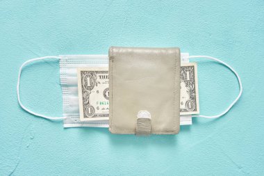 Deri cüzdanda tıbbi koruyucu maske ve bir dolar. Ekonomi ve salgın kavramı