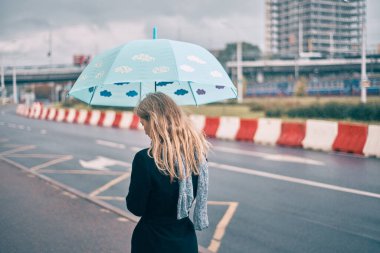 Sonbaharda şehirde şemsiyenin altında genç bir kız. Yağmur yağıyor.