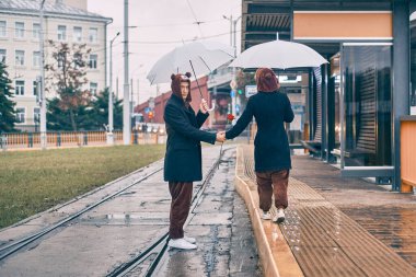 Genç çift yağmur altında yol boyunca yürür. Erkek ve kadın şemsiye altında ayı kostümlü