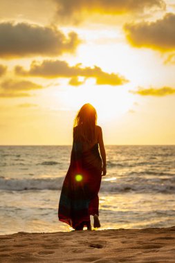 Gün batımında okyanusun sahilinde güzel genç bir kadın.