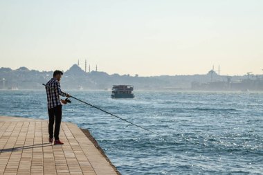 İstanbul, Türkiye. İnsan arka planda denizde balık yakalar. 