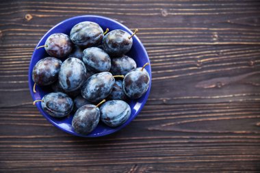 Ahşap zemin üzerinde mavi bir kasede mavi Erik.