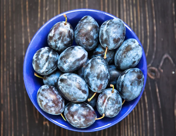 Blue plums in a blue bowl on wooden background.