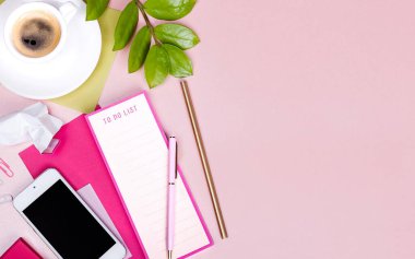 Planlı düz yatak, boş ataç tahtası, kalem, bir fincan espresso, akıllı telefon, yeşil yaprak, pembe arka grup