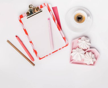 Planlı düz yatak, boş klip tahtası, pembe ofis kağıdı, bir fincan espresso, şekerler, beyaz arka plan.