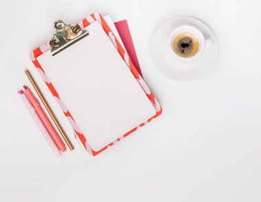 Planlı düz yatak, boş klip tahtası, pembe ofis kağıdı, bir fincan espresso, beyaz arka plan.