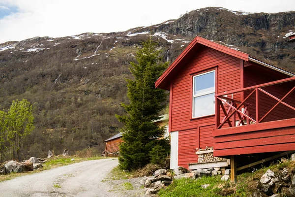 Small wooden red house on the hill in Norway. Gray rocks and green grass. Way to the hill.