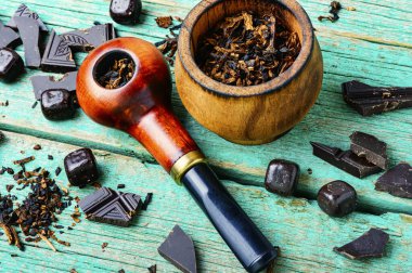 Sigara içmek için çikolata aromalı tütün. Tütünle dolu tütün piposu. Ahşap masada pipo.