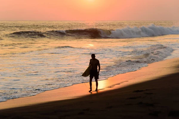 Silhouette of male surfer walking at beach with sunset