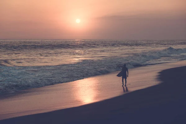 Silhouette of male surfer walking at beach with sunset