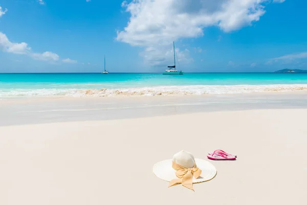 Sun hat and sandals on empty beach with turquoise sea