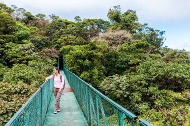 Young woman on hanging bridge in cloudforest, Monteverde, Costa Rica. clipart