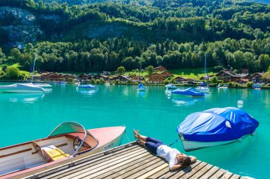 Woman laying on wooden pier in Village Iseltwald at Lake Brienz, Interlaken, Switzerland. clipart