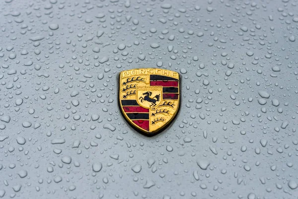 Emblema de la capucha del coche deportivo Porsche en gotas de lluvia sobre el fondo gris . — Foto de Stock