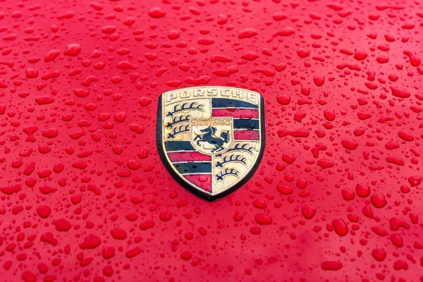 Cappuccio emblema di auto sportive Porsche in gocce di pioggia sullo sfondo rosso . — Foto Stock
