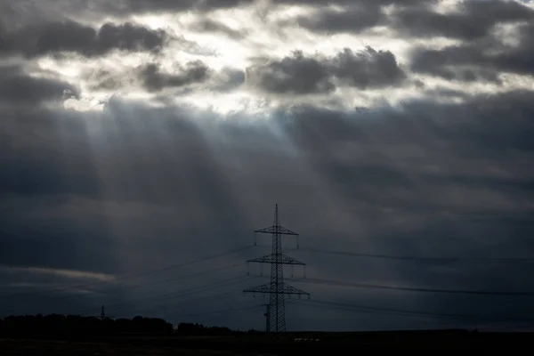 Rays of light making their way through dense clouds. Evening landscape. Agricultural land and power transmission lines. — Stock Photo, Image