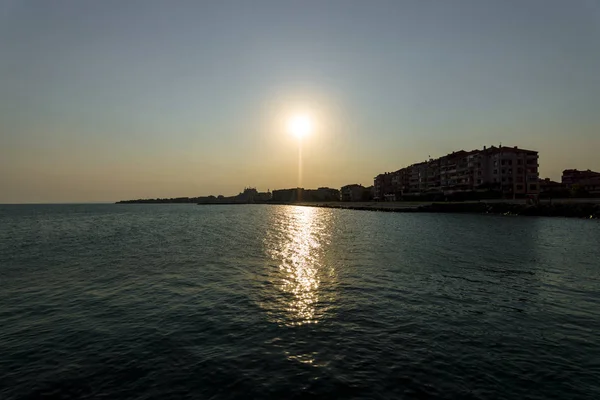 Zonsondergang in de zee. Silhouetten van gebouwen op het strand in tegenlicht. — Stockfoto