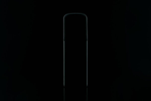 Silhouette of a black bottle with perfume on a dark background.