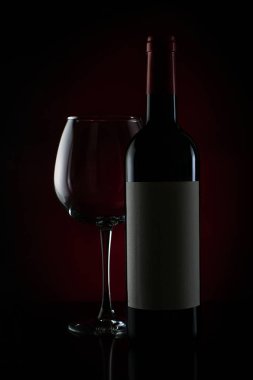 Siyah arka planda bir şişe şarap. Kırmızı arka planda kırmızı şarap ve cam..