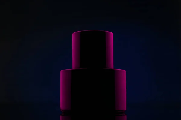 ブルーの背景にピンクの光の中で黒香水のボトル — ストック写真