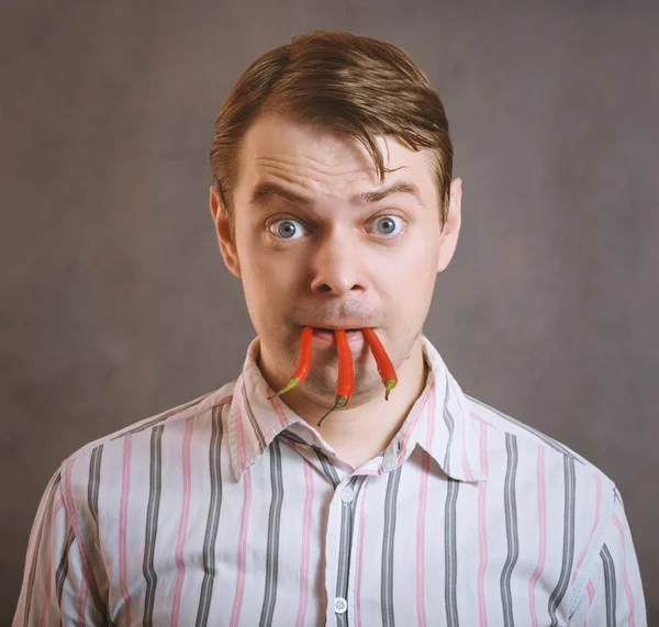 Mężczyzna trzyma papryczki chili w zęby. — Zdjęcie stockowe