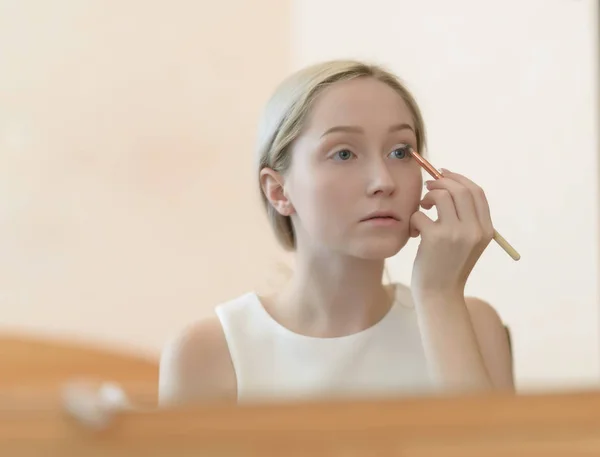 Mulher olhando no espelho durante a aplicação de maquiagem . — Fotografia de Stock