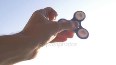 Mavi el spinner veya elinde dönen fidgeting getiriyor. Parlak gökyüzü arka plan. 