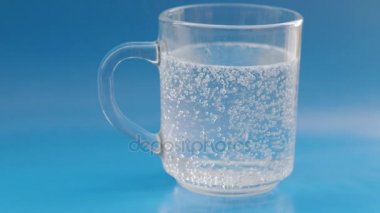 Bir bardak su mavi zemin üzerine efervesan hap. 