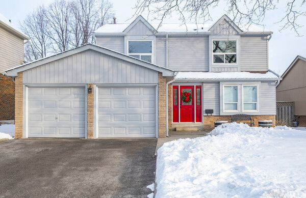 A Winter Scene of a Suburban Detached House with Grey Siding and Red Door Decorated with a Christmas Wreath