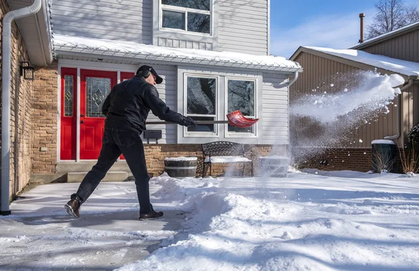 家の前に赤いシャベルで雪を取り除く男 — ストック写真