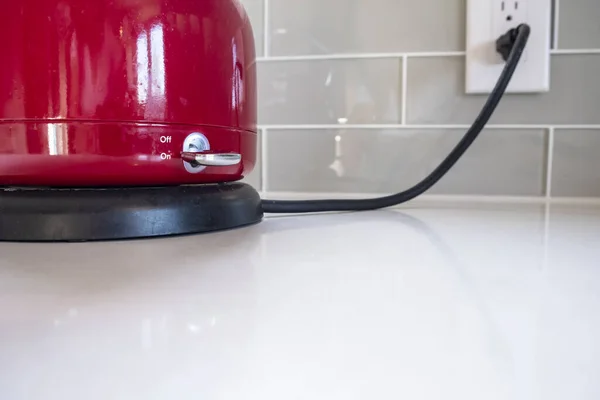 Red Electric Kettle Is Plugged In and Turned On to Boil Water on a White Quartz Counter Top in a Modern Kitchen