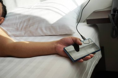 El kullanımı akıllı telefonlar tutuyor. şarj cihazı beyaz yatakta takılı, uyurken elektrik şarj tehlikesi