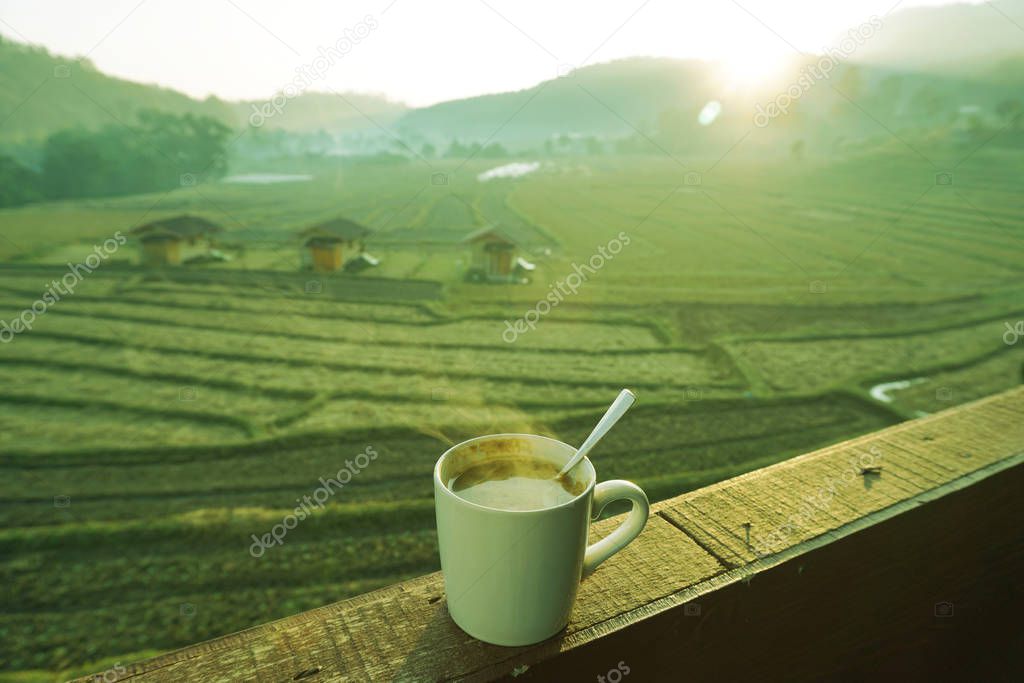 Hot coffee with smoke in white cup on wooden floors and natural rice fields, fresh atmosphere, sunlight in the early morning background