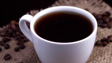 Beyaz kahve fincanı ve kahve çekirdekleri etrafa saçılmış, yakın plan kahve damlaları bir fincana dökülüyor. yavaş çekim