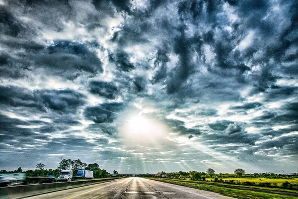 Autostrada attraverso il paesaggio di campagna con cieli drammatici e sole ra — Foto Stock