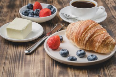 Kahve fincanı, kruvasan, beyaz kasede böğürtlen ve tereyağı.