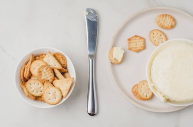 Beyaz bir kasede beyaz bir sırtında bıçakla peynir ve kraker.