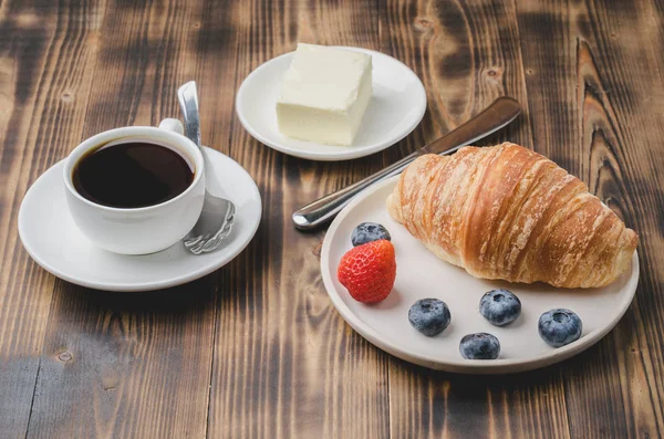 Coffee cup, croissant with berries in white bowl and butter on w