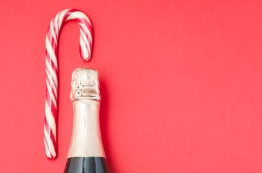 Kırmızı arka planda bir şişe şampanya ve baston şeker..