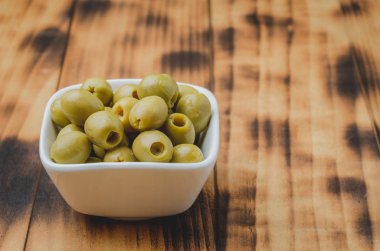 Ahşap zemin üzerinde beyaz bir seramik kasede yeşil zeytinler