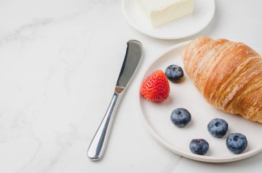 Beyaz kasede böğürtlenli kruvasan ve beyaz stonda yağ bıçağı.