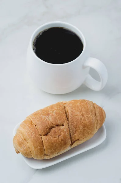 Caneca branca com café preto e croissant na mesa de pedra branca . — Fotografia de Stock