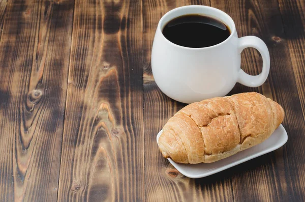 Caneca branca com café preto e croissant no fundo de madeira w — Fotografia de Stock