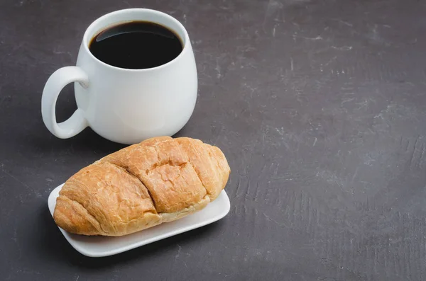 Caneca branca com café preto e croissant em backgrou de pedra escura — Fotografia de Stock