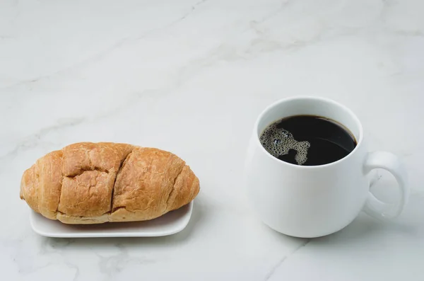 Caneca branca com café preto e croissant na mesa de pedra branca . — Fotografia de Stock