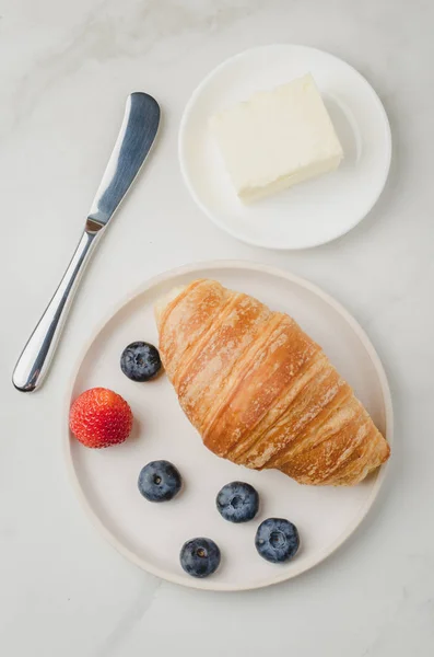 Croissant con bayas en tazón blanco y cuchillo de mantequilla en t blanco — Foto de Stock