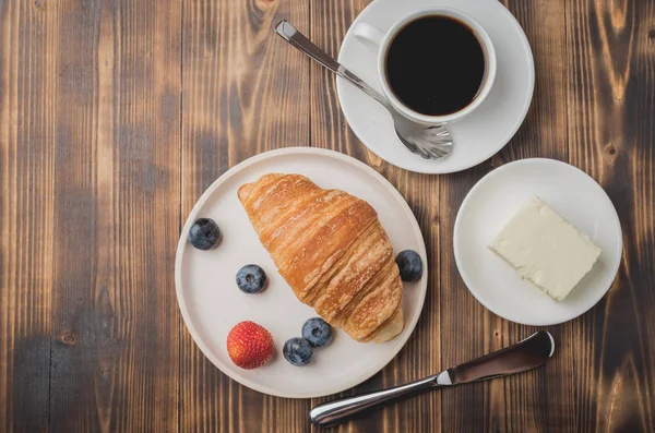 Coffee cup, croissant with berries in white bowl and butter knif