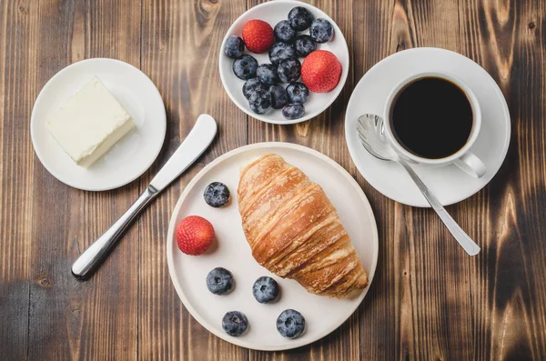 Xícara de café, croissant com bagas em tigela branca e faca de manteiga — Fotografia de Stock