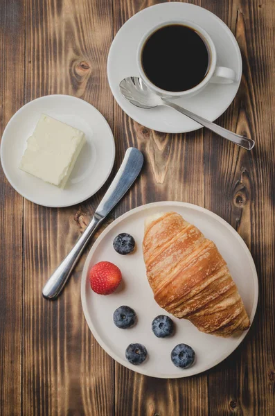 Coffee cup, croissant with berries in white bowl and butter knif