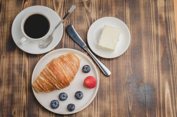 Xícara de café, croissant com bagas em tigela branca e faca de manteiga — Fotografia de Stock